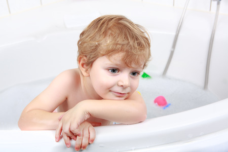 Adorable  blond toddler boy having fun with water by taking bath in bathtubの写真素材