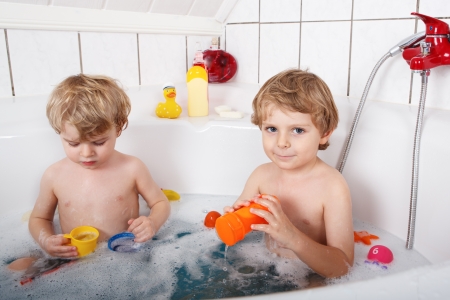 Two little twins boys having fun with water by taking bath in bathtubの写真素材