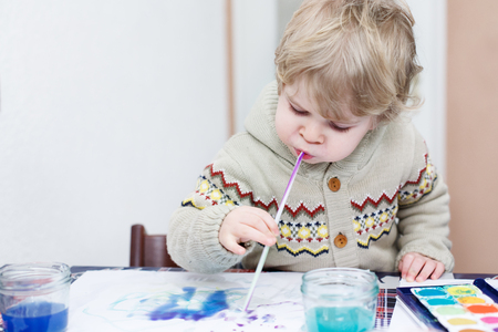 Lovely toddler boy having fun indoor, painting with different paints colorsの写真素材