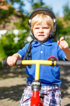 Cute little boy of two years having fun on his bicycle in summer gardenの写真素材