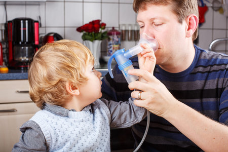 Little boy and his father making inhalation with nebuliser in home kitchen