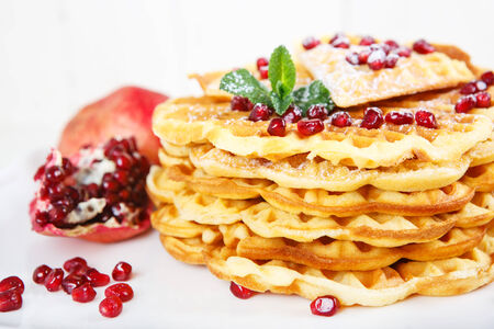 Crisp golden fresh baked waffle topped with pomegranate on white tableの写真素材