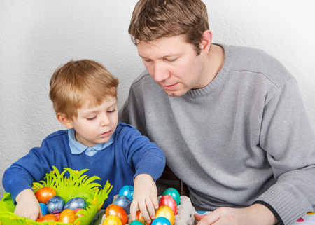 Little toddler boy and his mother having fun with preparing eggs for Easter egg hunt, traditional action in Germany for Eastern holiday, indoorsの写真素材