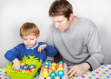 Little toddler boy and his mother having fun with preparing eggs for Easter egg hunt, traditional action in Germany for Eastern holiday, indoorsの写真素材