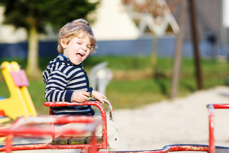 Little toddler boy having fun on old carousel on outdoor playground.の写真素材