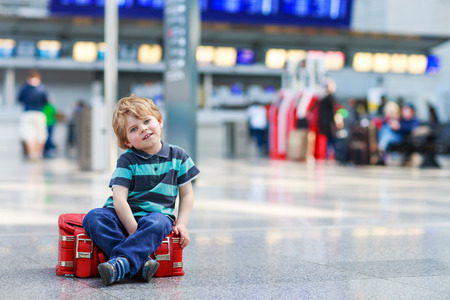 Blond boy of 2 years sitting on suitcase at the airport, indoors and waiting for going on vacations.の写真素材