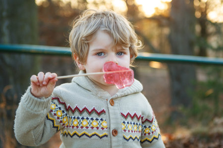 Portrait of beautiful little boy of 2 with big candy, outdoors. Evening light.