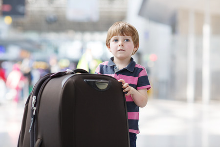 Blond boy of 4 years with huge suitcase at the international airport, indoors and waiting for going on vacations.の写真素材