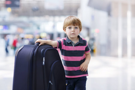 Blond boy of 4 years with huge suitcase at the international airport, indoors and waiting for going on vacations.の写真素材