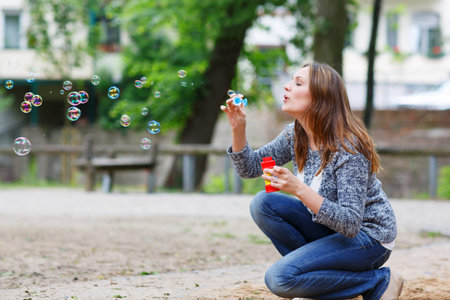 Beautiful young woman playing with soap bubbles in park