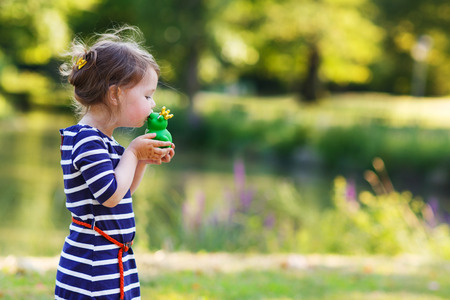 Adorable little girl giving a kiss to rubber frog. Outdoorsの写真素材
