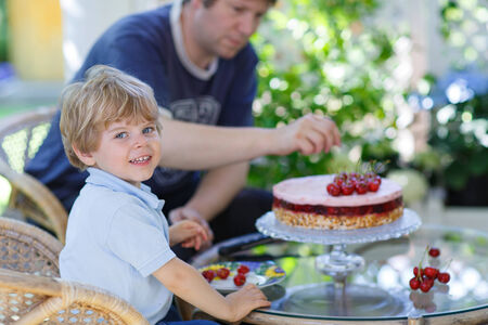Little boy and his father eating cherry cakeの写真素材