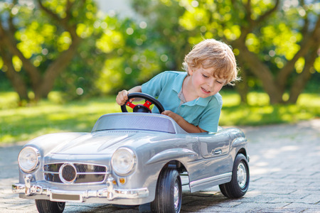 Happy little boy driving big toy car and having fun, outdoors.の写真素材