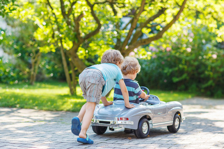 Two happy children playing with big old toy car in summer garden, outdoors.の写真素材