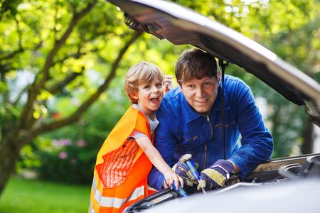 Young father teaching his little son in safety uniform to repair some parts in family car.の写真素材