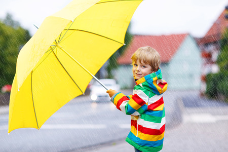 Adorable toddler child with yellow umbrella and colorful jacket outdoors at rainy dayの写真素材