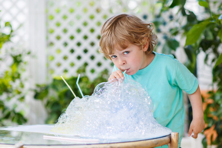 Happy little boy having fun and making experiment with colorful soap bubbles and water, outdoors.の写真素材