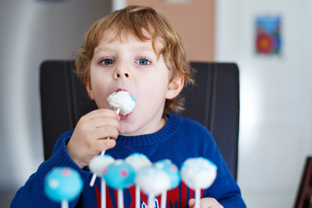 Little blond boy eating colorful cake pops, indoors.の写真素材