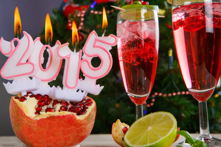 Two glasses with red pomgranate champagne and burning candles 2015 with christmas tree on background