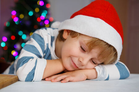 Little boy in santa hat with christmas tree and lights on background, sleeping and dreamingの写真素材