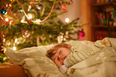 Little cute blond boy sleeping under Christmas tree and dreaming of Santa at home, indoorsの写真素材