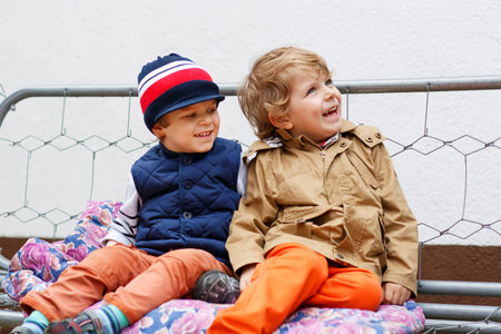 Two happy boys on swing in spring garden. Having fun and smiling.