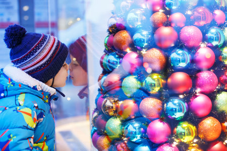 Adorable little boy looking through the display window at Christmas decoration in the shop