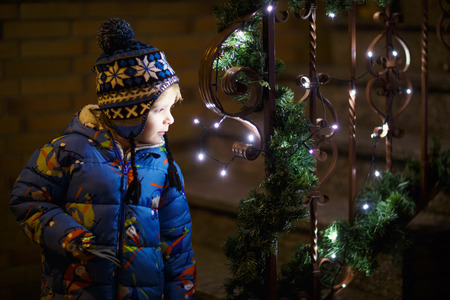 Little cute child standing outdoors at Christmas time with illuminated lights.の写真素材