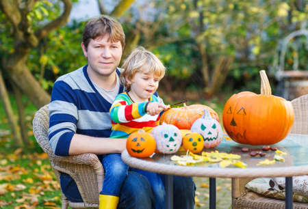 Adorable little child and his father making jack-o-lantern for halloween in autumn garden, outdoors. Family having fun togetherの写真素材