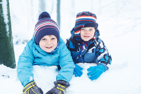 Two cute little twin boys having fun with snow in winter forestの写真素材
