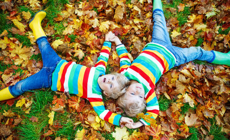 Two little kid boys lying in autumn leaves in colorful clothing. Happy siblings having fun in autumn park on warm day.の写真素材