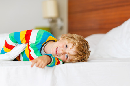 Adorable kid boy relaxing and resting after sleeping in his white bed in colorful pajama with stripes. Indoor.の写真素材
