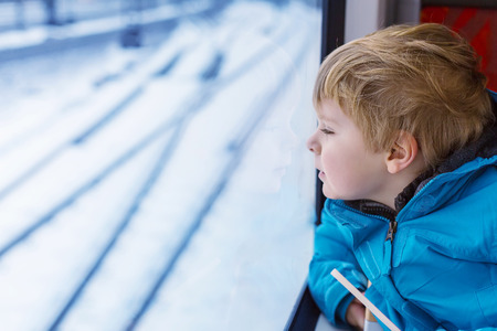 Adorable little kid looking out train window outside, while it moving. Going on vacations and traveling by railway in winter.の写真素材