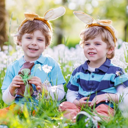 Family of two siblings: Little kid boys wearing Easter bunny ears at spring green grass and blooming...