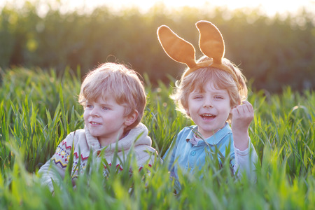 Two children playing with Easter bunny ears playing in green grass on Easter holidayの写真素材