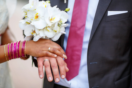 Beautiful indian bride and caucasian groom, after wedding ceremony. hands of man and woman with rings and traditional indian jewelryの写真素材