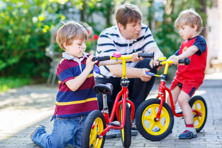 Father teaching two little kid boys to repair chain on bikes, showing to change a wheel. Family...