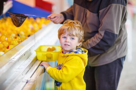 Little cute kid boy playing game with rubber ducks on fair or amusement park with his father.の写真素材