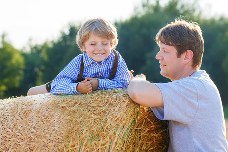 Young father and his little son having fun on yellow hay field in summer. Happy family of two. Active outdoors leisure with children on warm summer day.の写真素材