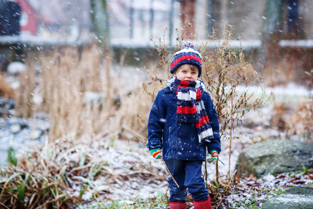 Winter portrait of kid boy in colorful winter clothes, outdoors during snowfall. Active outoors leisure with children in winter on cold snowy daysの写真素材