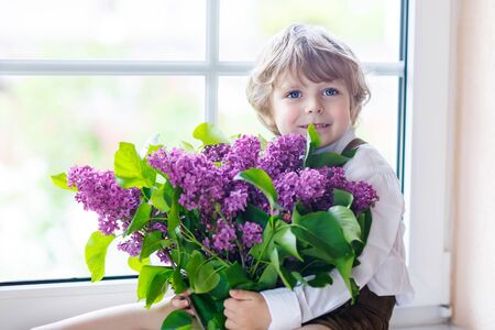 Adorable smiling little boy with blooming purple lilac flowers, indoor. Mother's day, father's day or valentine's day concept.の写真素材