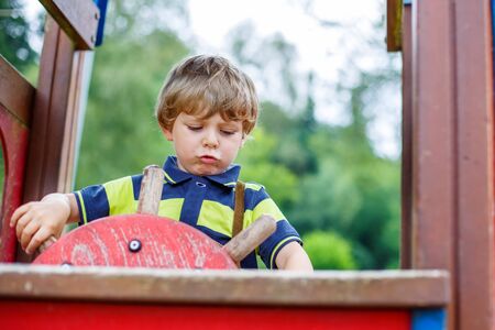 Funny kid boy pretends driving an imaginary car on children playground, outdoors. On warm summer day.の写真素材
