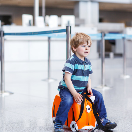 Blond boy of 2 years sitting on suitcase at the airport, indoors and waiting for going on vacations.の写真素材