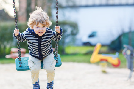 Adorable toddler boy having fun chain swing on outdoor playground.の写真素材
