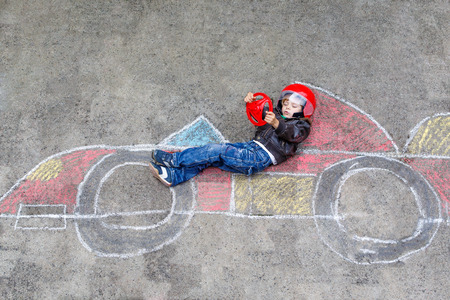 Funny kid boy having fun with race car picture drawing with colorful chalks. Creative leisure for children outdoors in summerの写真素材