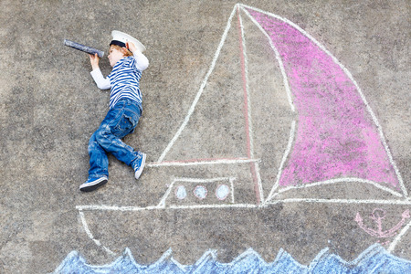 Cute little boy sailing on ship or boat picture drawing with chalk. Creative leisure for children outdoors in summerの写真素材