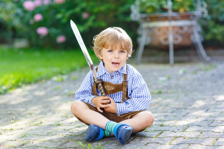 Portrait of little blond kid boy with toy sword, outdoors. On warm sunny summer day.の写真素材