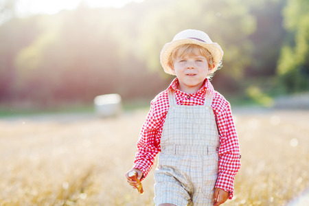 Little toddler boy  walking happily through wheat field near  hay stack or bale. Active outdoors leisure with children on warm summer day.の写真素材
