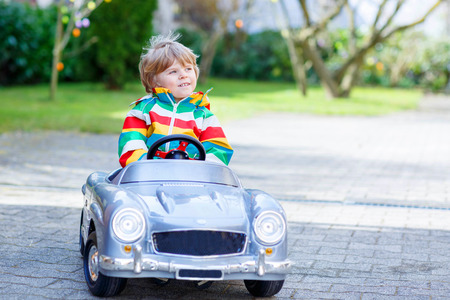 Cute funny boy driving big toy old vintage car and having fun, outdoors. Active leisure with kids outdoors  on warm spring or autumn day.の写真素材