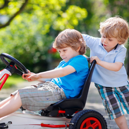 Two funny twins boys having fun with toy race car in summer garden, outdoors. Adorable brother pushing the car with another child. Outdoor games for children in summer concept.の写真素材